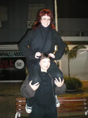 Duas integrantes, uma nos ombros da outra, à noite na rua